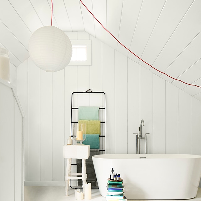 Salle de bains blanche lumineuse avec des murs et un plafond en planches à feuillure, luminaire suspendu blanc en forme de globe et baignoire contemporaine autoportante.