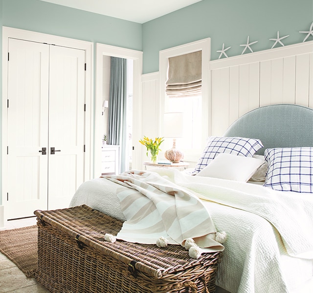 Light blue bedroom walls with white built in desk, a large bed with light and dark blue pillows and comforter.