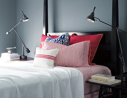 Sleek, Wolf Gray-painted bedroom with black bedframe, red and white bedding, two swing-arm lamps, and stacks of books. Sleek, Wolf Gray-painted bedroom with black bedframe, red and white bedding, two swing-arm lamps, and stacks of books.
