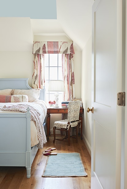 Cream bedroom with sky blue ceiling and a matching blue bedframe including light pink curtains and pillows.