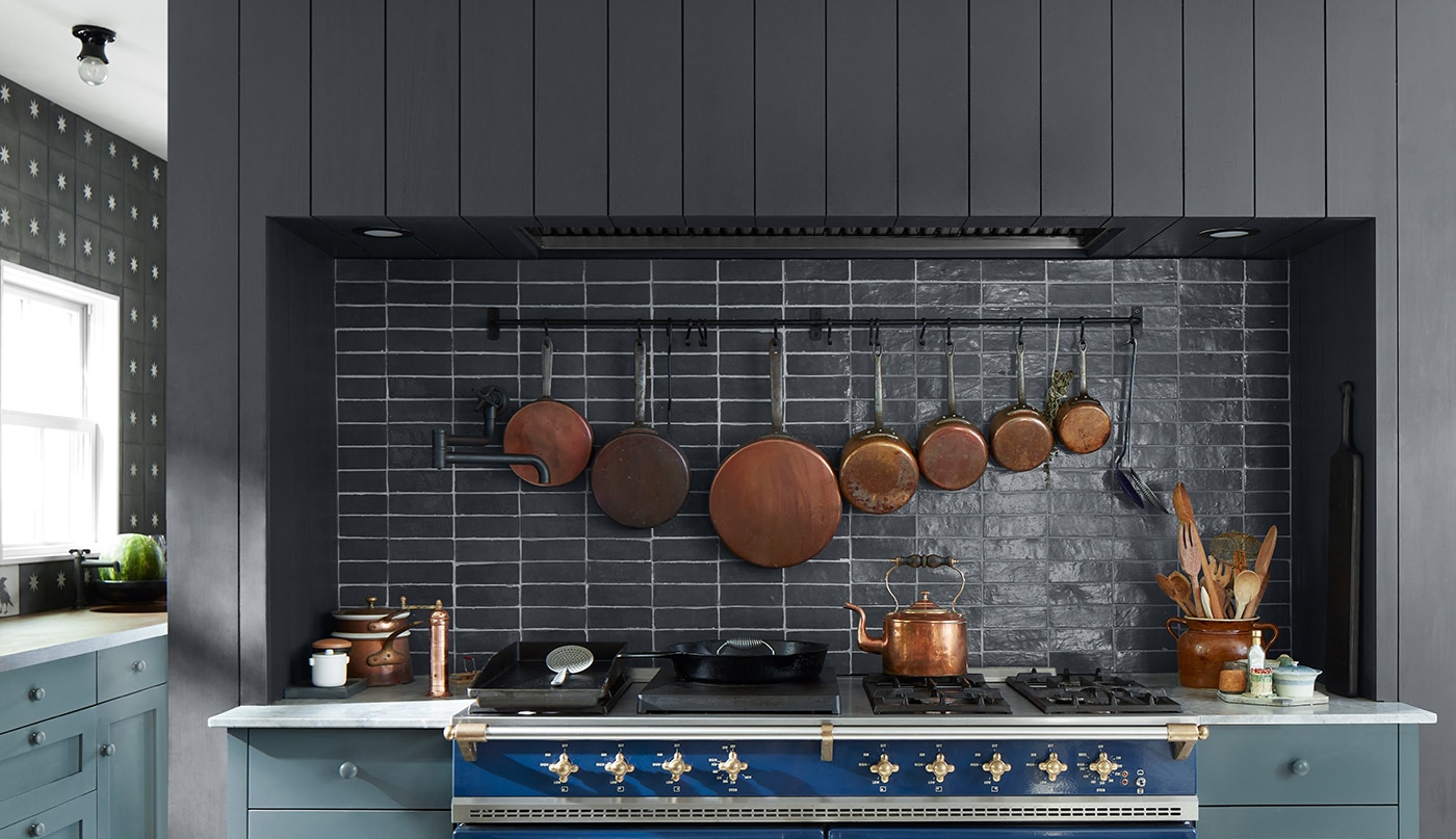 A warm, inviting kitchen with blue-painted cabinets, a black shiplap wall and black backsplash, a white ceiling, blue stove, and wood table and chairs.