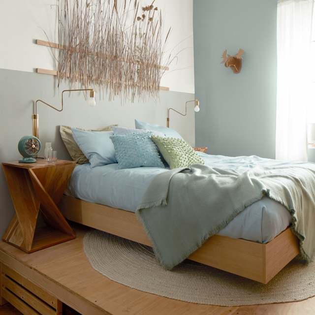A bed with blue and light green bedding on a light wooden platform in a room painted in light blue, gray, and white.