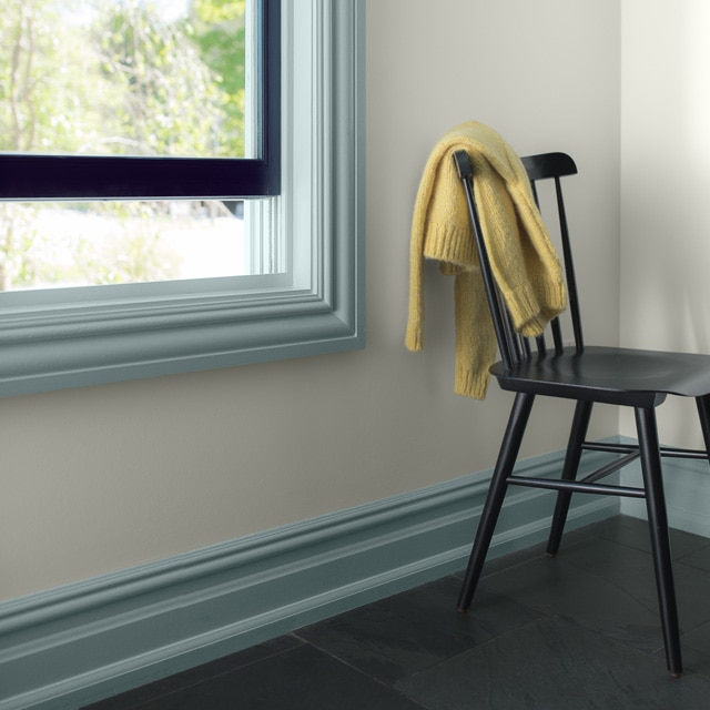 A white-painted room corner with light blue trim and dark navy mullion, and a black spindle chair with a yellow throw.