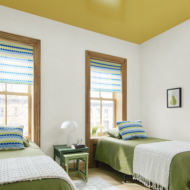 A rich ochre painted ceiling with hints of green and yellow makes a fun statement in this bedroom with white walls, natural wood trim, and twin beds with green and white bedding.