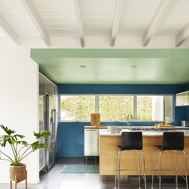A white painted shiplap ceiling with beams and a white wall leading to a modern kitchen with blue painted walls and a green ceiling.