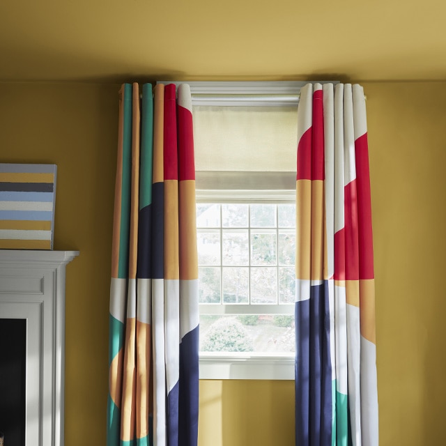 A rich ochre painted wall and ceiling with hints of green and yellow, a white fireplace mantel and trim, and colorful patterned curtains.