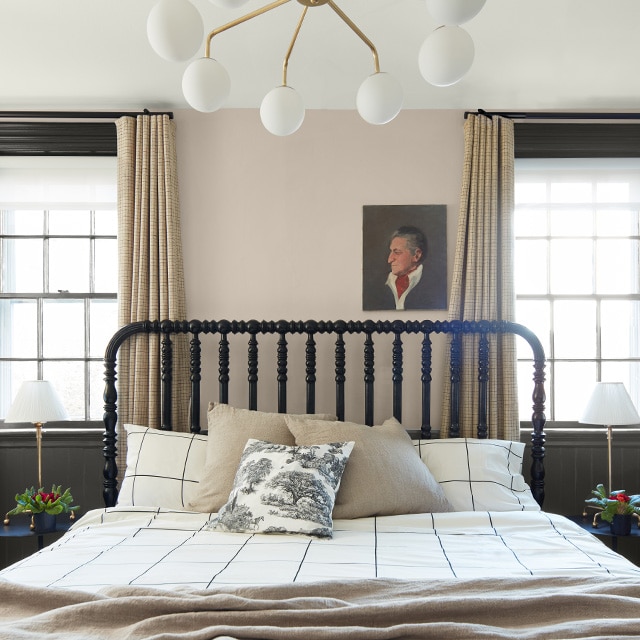 Chambre à coucher avec mur à deux tons – beige et gris anthracite – plafond blanc, deux fenêtres à rideaux beiges et literie grise à carreaux.