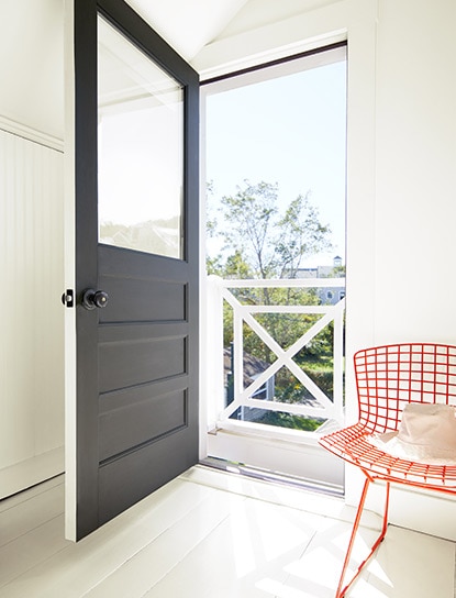 Une porte d'entrée noire s'ouvre sur un vestibule aux murs blancs avec une chaise métallique rouge.