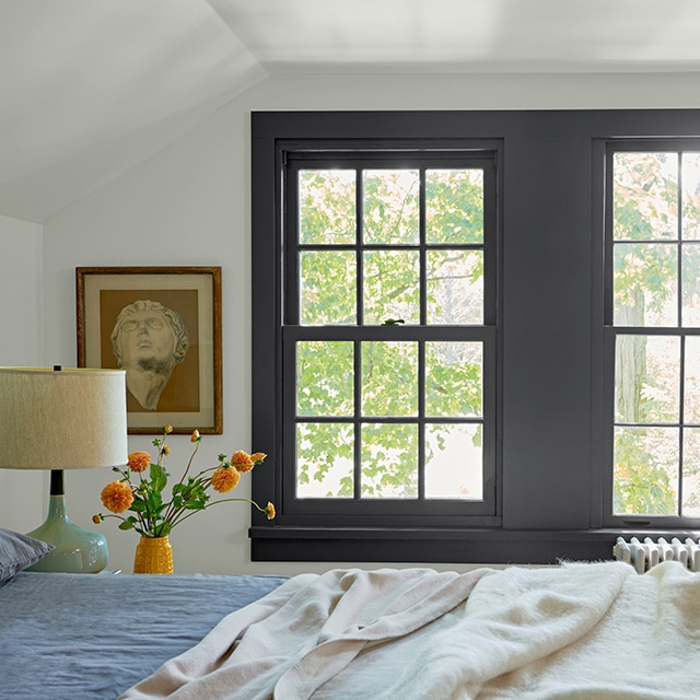 A bedroom with white-painted walls and ceiling, black trimmed windows, and blue and white bedding.