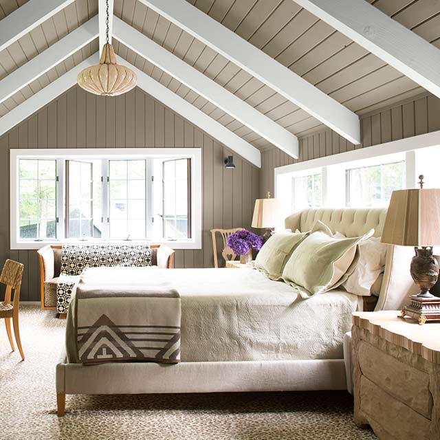 A master bedroom with gray-painted walls and vaulted ceiling, white wood beams and trim, and neutral coloured décor.