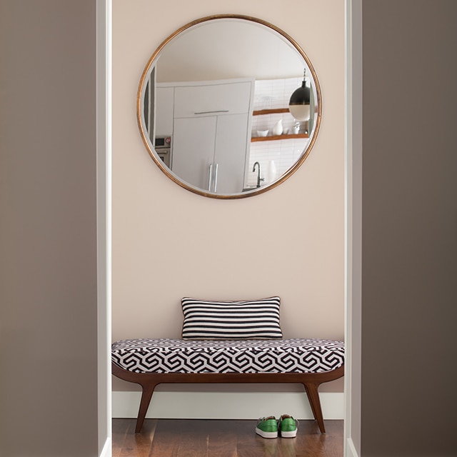A contemporary hallway in light pink paint, and greige walls, with a modern bench, and circular wall mirror.