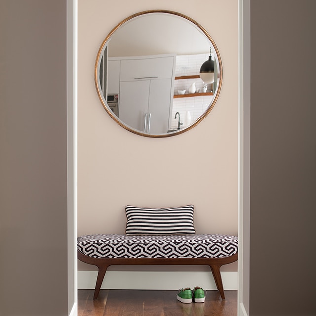 Un couloir de style contemporain peint en rose clair arborant des murs grèges, un banc moderne et un miroir mural circulaire.