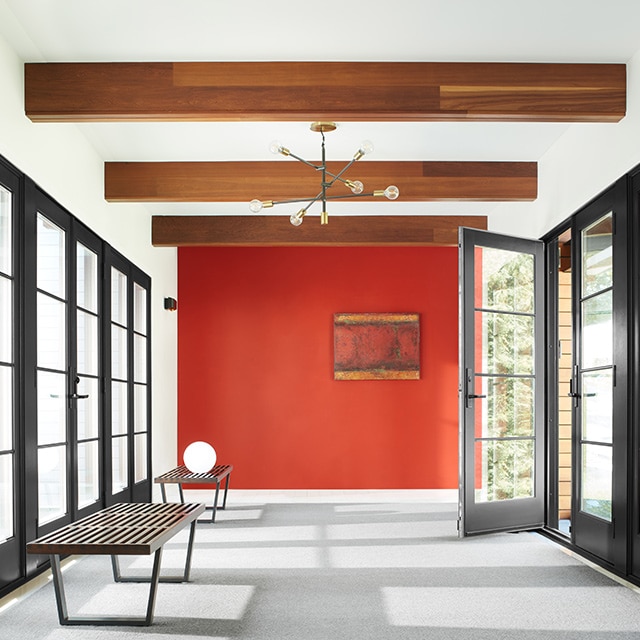 A white-painted hallway with a red accent wall, wood beam ceiling, black-trim windows and door, and modern furnishings.