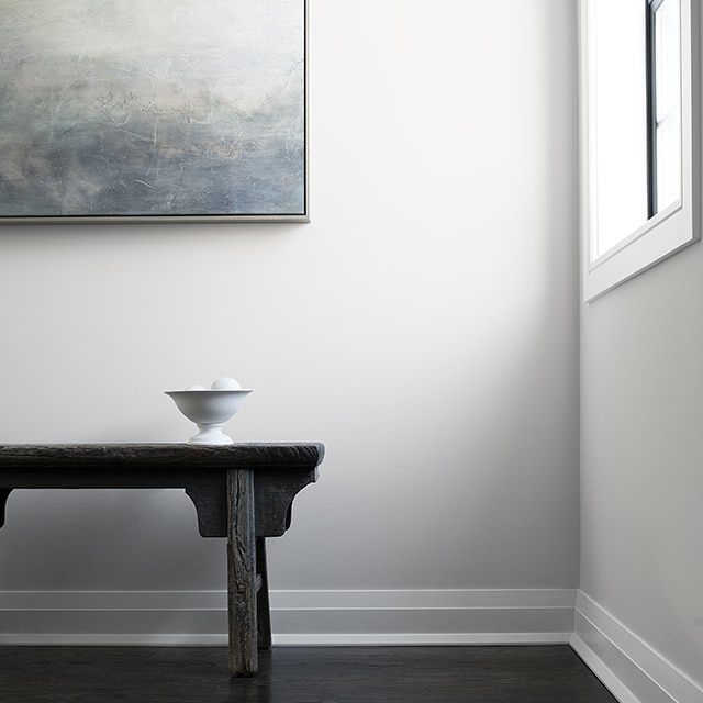 A hallway with white walls and trim, a black wooden bench, and contemporary art.