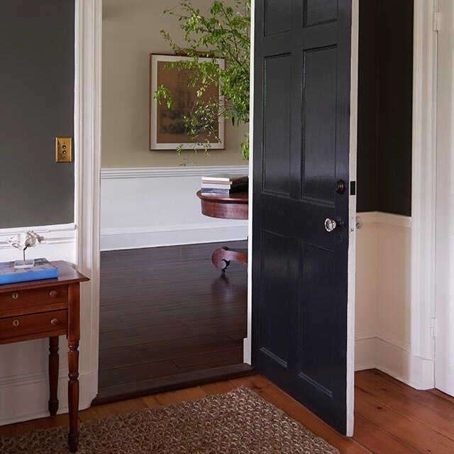 Une porte ouverte peinte en noir menant à un couloir aux teintes neutres.