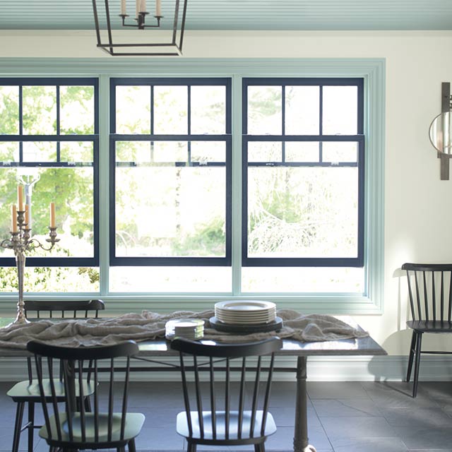 A dining room with window trim paint in light blue and navy, a light blue ceiling, white walls, spindle back chairs, and dining room table.