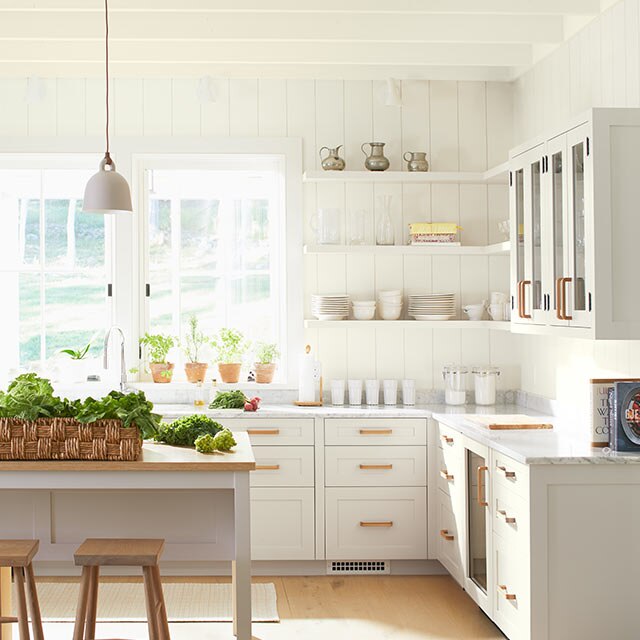 Une cuisine entièrement peinte en blanc présentant des armoires blanches, un îlot surmonté d’un bloc de boucher et des luminaires suspendus.