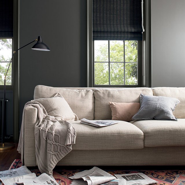 Charcoal gray-painted walls with matching charcoal gray window trim, beige couch, off-white throw, and patterned rug.