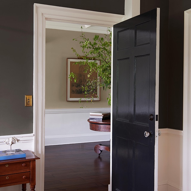A room with soft black painted upper walls and white lower walls with white trim and an open black door leading to a hallway in neutral hues.