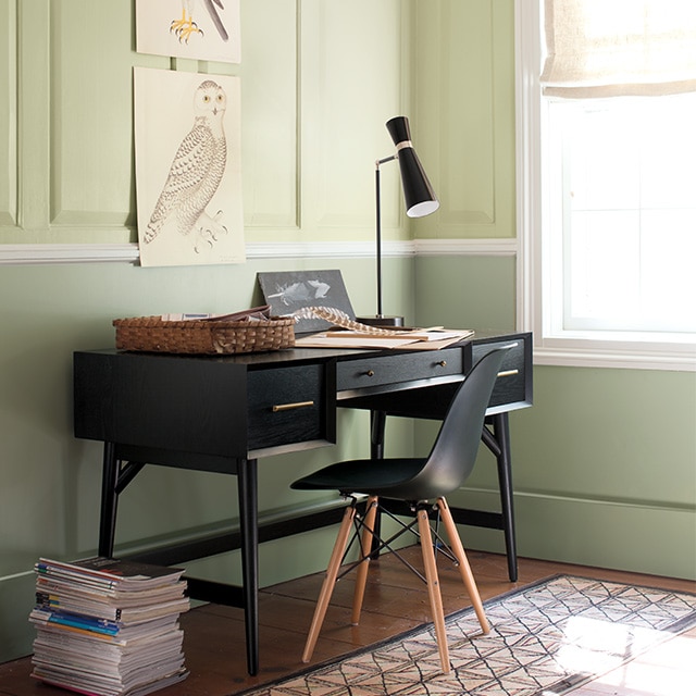 Pretty two-tone green painted corner walls with wainscotting on the upper walls, white trim, and a black desk and chair.