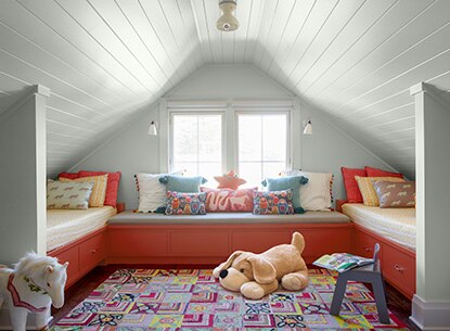 Kids' room with white shiplap walls, two beds and sofa atop red drawers with accent pillows, stuffed toys and small blue chair.