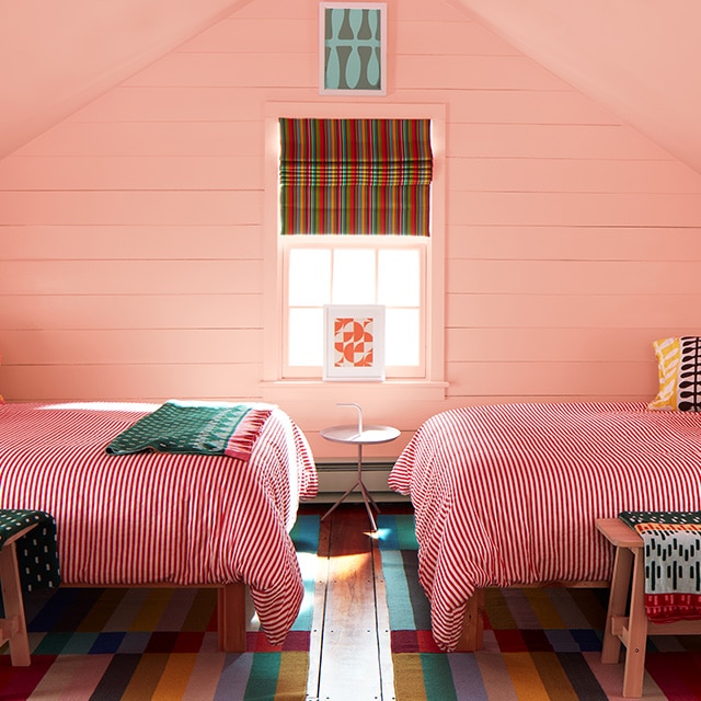A bedroom painted a pink-orange pastel hue on the shiplap walls and vaulted ceiling features colorful bedding and decor, mixing stripes and patterns.