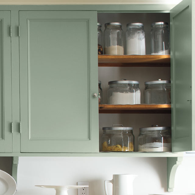 Light green cabinets add a soft glow as a backdrop to a dining table.