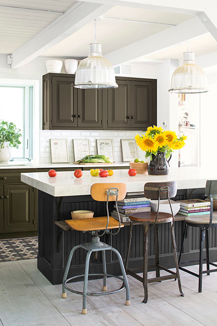 An airy industrial style kitchen taps into deep colors, from a black based kitchen island to deep green-brown cabinetry.