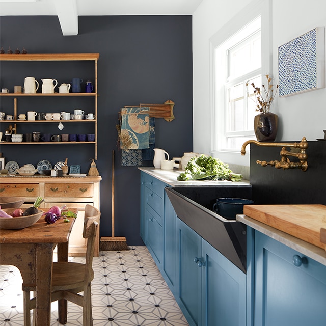 Una cocina con estilo de tradición inglesa con gabinetes pintados en color azul, una pared de acento pintada en azul marino y muebles de madera.