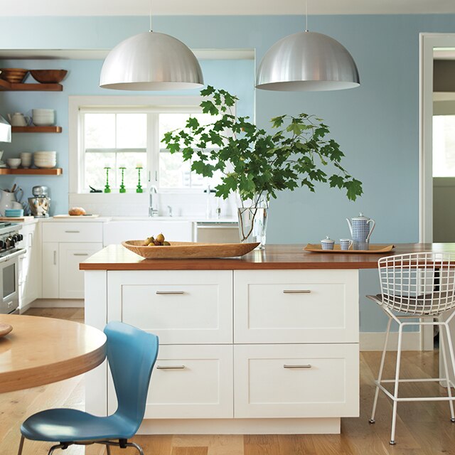 A bright and airy contemporary kitchen with white-painted cabinets and center island with a wood top, and light blue walls.