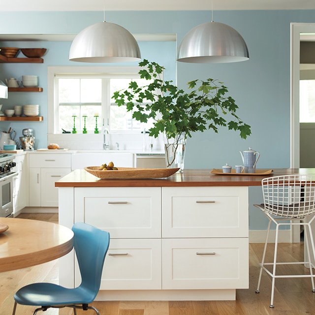 Una cocina contemporánea luminosa y espaciosa con gabinetes pintados de blanco e isla central con encimera de madera y paredes en azul claro.