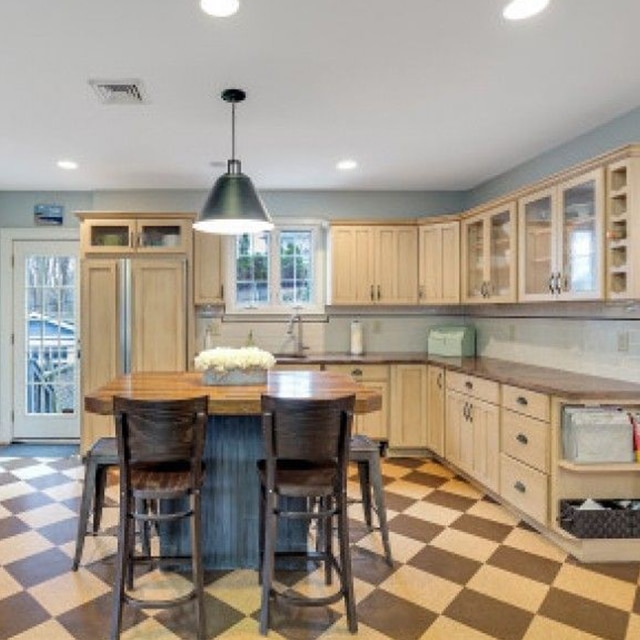 A kitchen with off-white painted cabinets, light-blue walls, a center wood island, and a checkboard floor before a makeover.