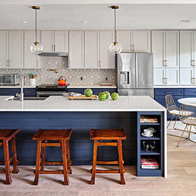 The same kitchen after a makeover, with white-painted upper cabinets, dark blue lower cabinets and island, white countertops, and a small dining set.