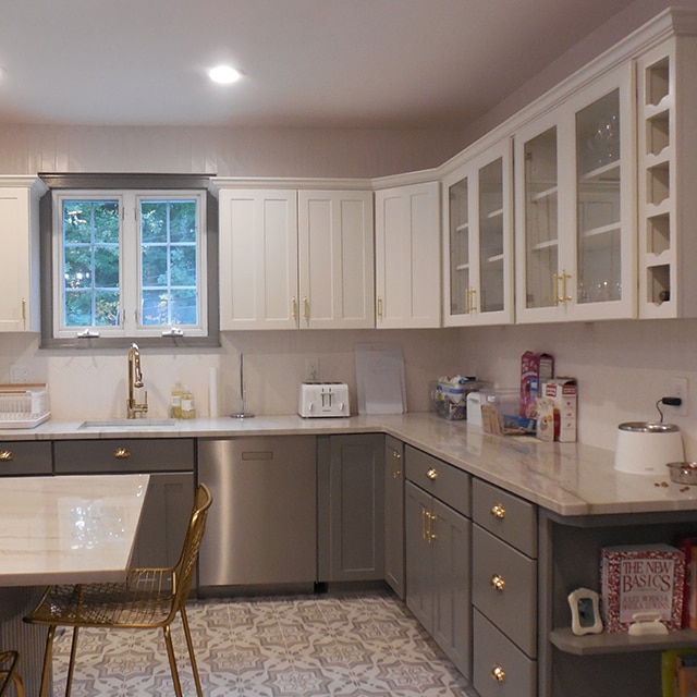 The same kitchen after a makeover, with white-painted upper cabinets, dark gray lower cabinets and island, white countertops and white walls.