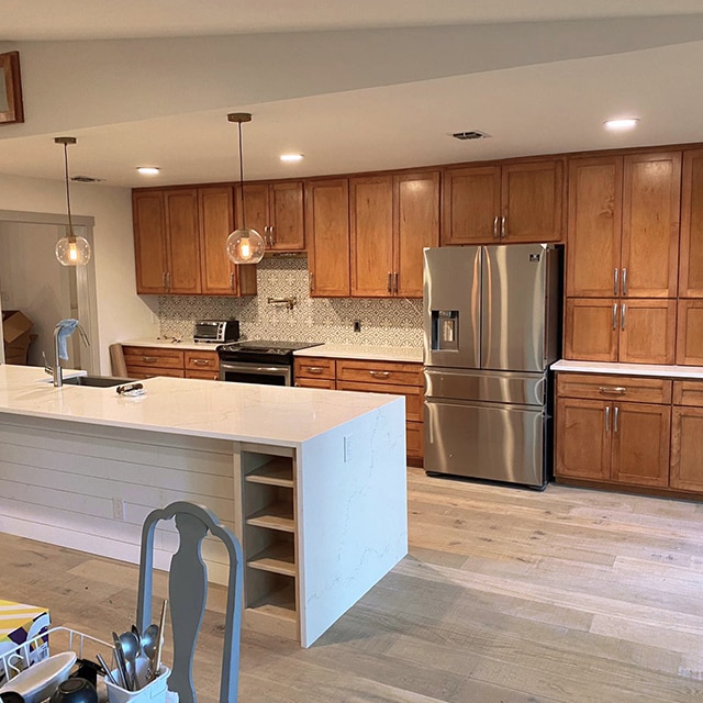 Una cocina luminosa y abierta con gabinetes de madera en una pared y una gran isla blanca con un lavabo antes de una renovación completa.