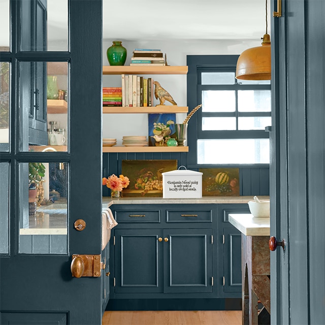 Pretty teal-painted doors open to a kitchen with teal cabinets, trim and backsplash, and floating wood shelves against a light gray wall.