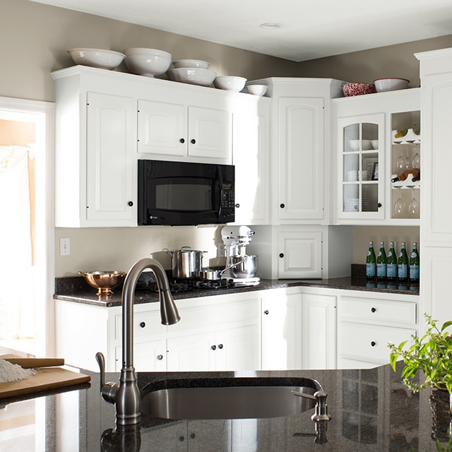 La misma cocina después de una renovación completa, con nuevos gabinetes pintados de blanco, encimeras negras y electrodomésticos.