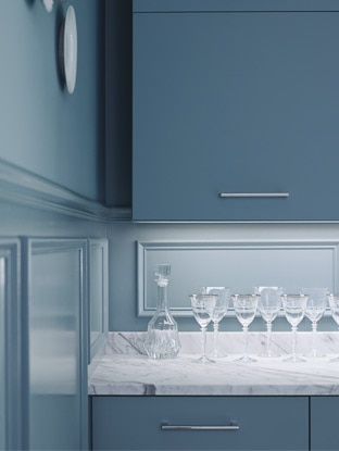 Monochromatic blue cabinets and blue walls are highlighted by a white marble countertop set with wine glasses.