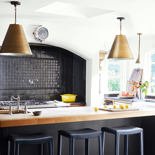 Cuisine blanche avec dosseret à carreaux noirs, îlot noir avec comptoir blanc et luminaires suspendus.