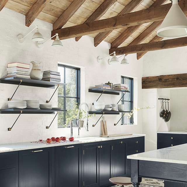 Una cocina abierta grande con paredes pintadas de blanco, un techo abovedado de madera, y hermosos gabinetes inferiores pintados en un llamativo color azul de mezclilla.