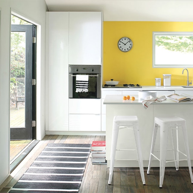 Une cuisine arborant un mur d’accent peint en jaune, des armoires et des comptoirs blancs, une cuisinière autonome, une surface de cuisson et un évier. 