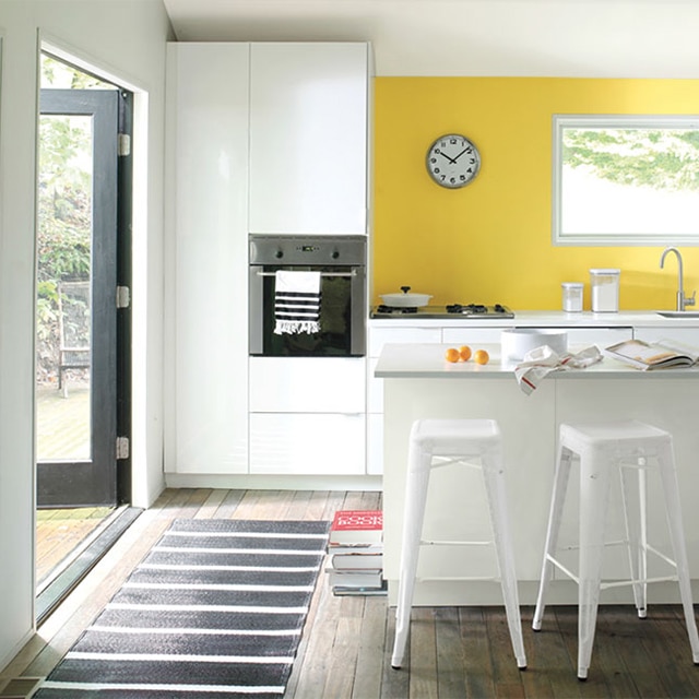 Cocina con pared de acento pintada de amarillo, mesadas y gabinetes blancos, horno independiente, estufa y lavabo.