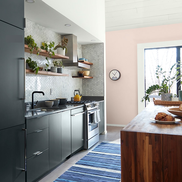 Petite cuisine accueillante avec armoires gris anthracite, dosseret à carreaux gris perle, mur d’accent rose et petit tapis à rayures bleues.