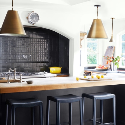 Close up of a kitchen with black tile backsplash, gas range top, and island counter with sink.