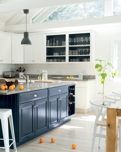 Une cuisine arborant un îlot peint en bleu foncé, des armoires blanches, une table en bois et divers tabourets blancs.
