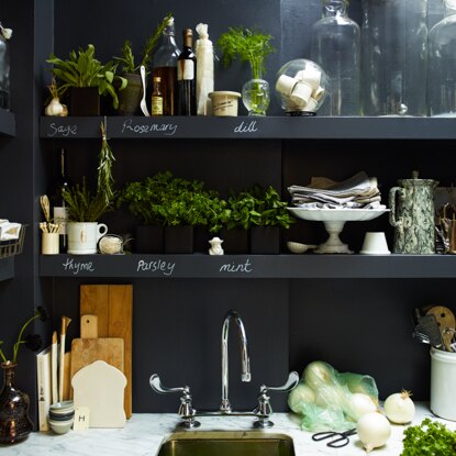 Close up of kitchen shelves painted with black chalkboard paint, used to display herbs, various cutlery, and cutting boards.