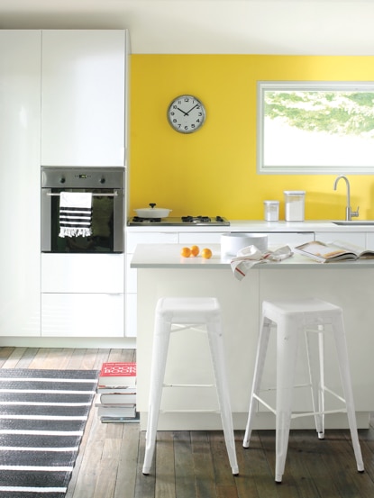 Kitchen with yellow-painted accent wall, white counters and cabinets, stand-alone oven, stove top, and sink. 