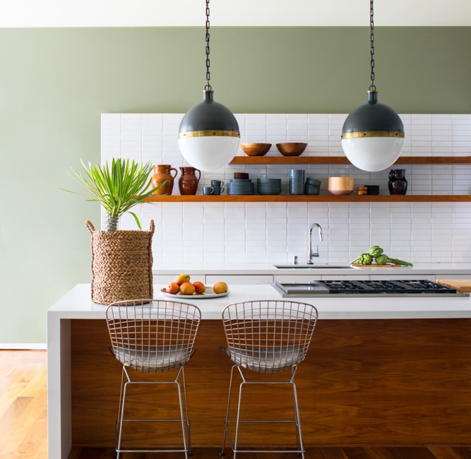 Modern kitchen with wooden counters, white countertops, green-painted walls, and metal stool seating.