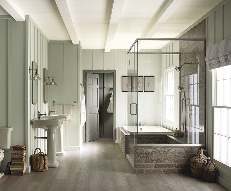 Neutral green bathroom with marble shower and tub, hardwood floors, Kohler finishes and wood panels