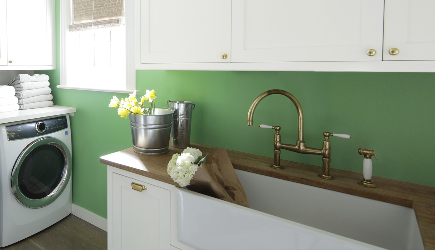 Une salle de lavage arborant des armoires blanches, un mur vert, un comptoir en bois ainsi qu’une laveuse et une sécheuse blanches.